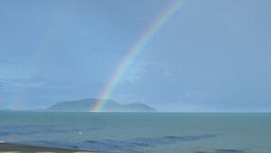 A beach with a rainbow over the ocean and a distant island.