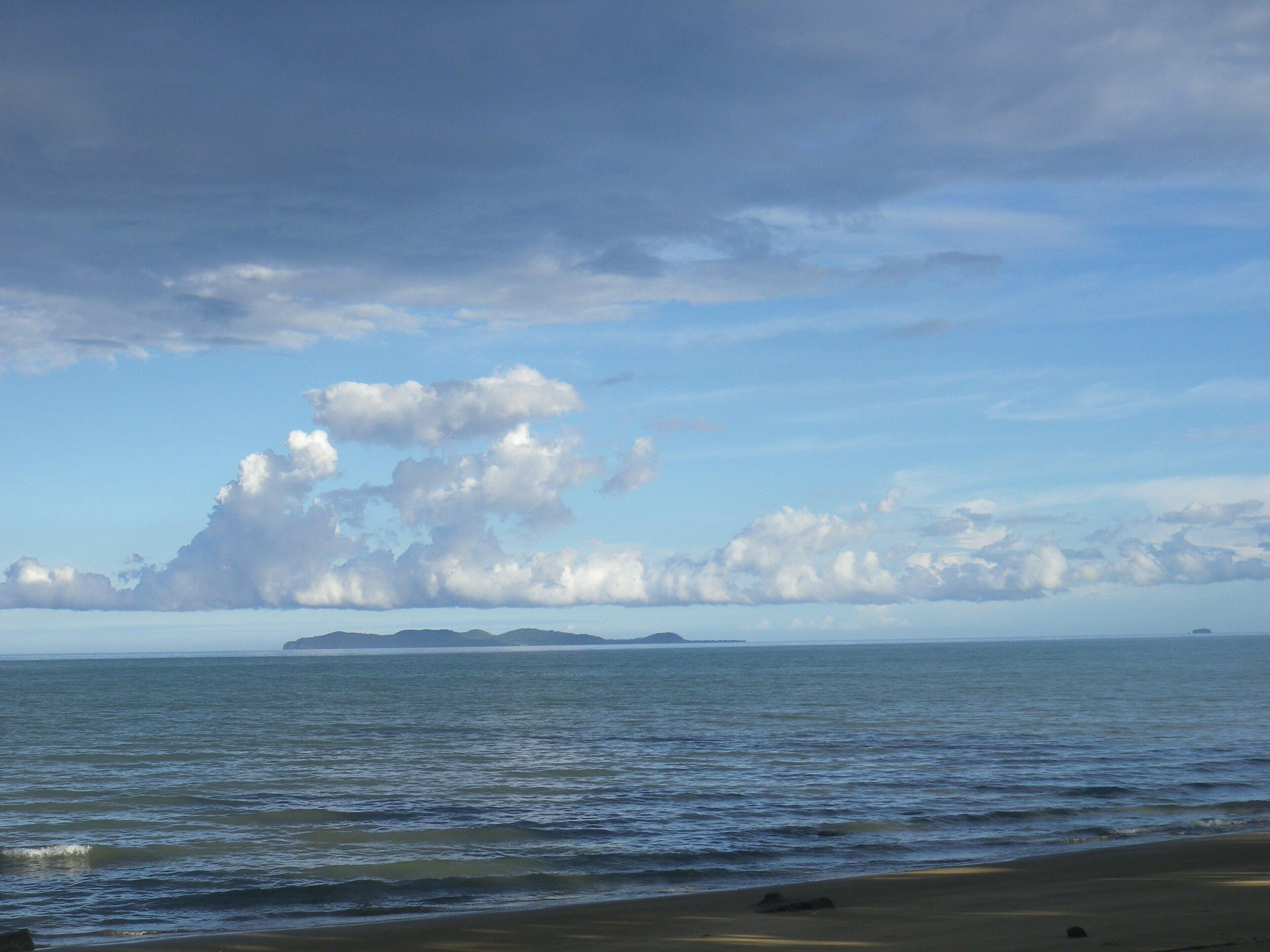 En strand med roligt vand, en sandet kystlinje og fjerne øer under en let overskyet himmel.