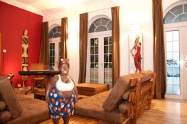 A spacious living room with a red accent wall, a piano, and a large window with curtains.