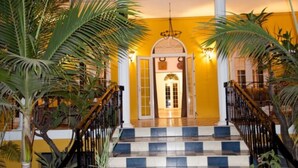 A grand staircase with a checkered floor leading to a doorway, flanked by palm trees and a yellow wall. - Villa Anakao (Port Louis)