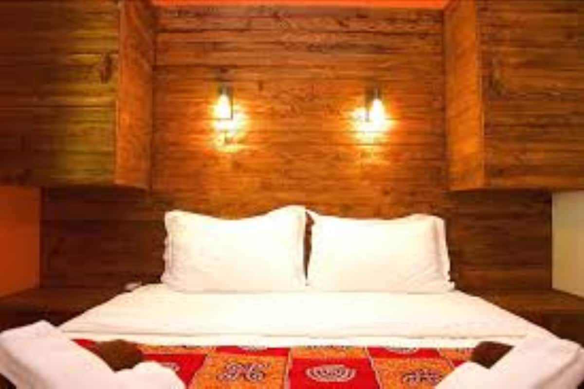 A wooden-paneled room with a bed, two wall-mounted lights, and a red patterned bedspread.