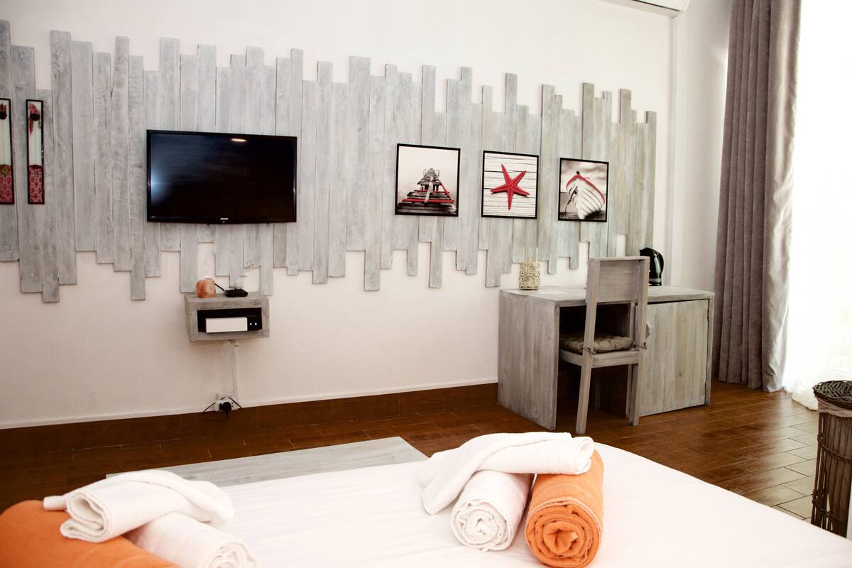 A hotel room with a bed, a desk, a chair, a TV, and artwork on the wall.