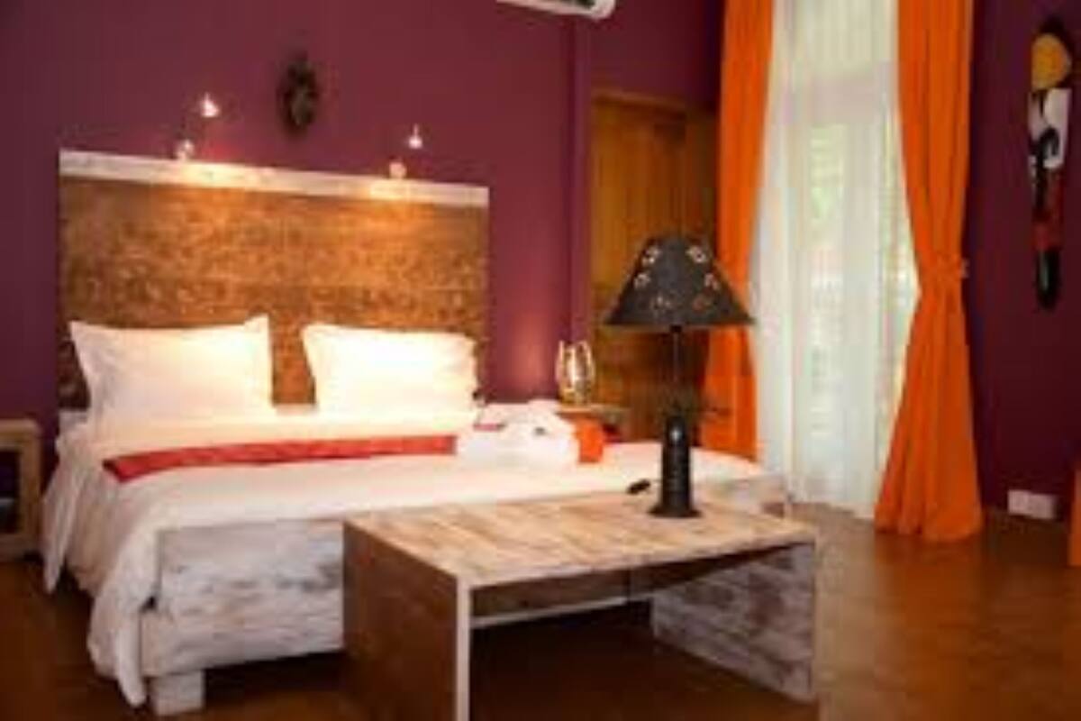 A bedroom with a wooden headboard, a bed with white bedding, a bedside table with a lamp, and orange curtains.