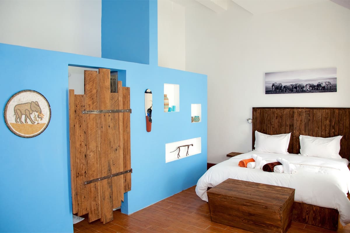 A bedroom with a blue accent wall, a wooden door, a bed with white bedding, and a wooden headboard.