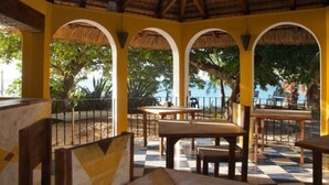 A covered outdoor seating area with tables and benches, a thatched roof, and views of the sea and trees. - Villa Anakao (Port Louis)