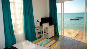A room with a bed, a desk with a television, and a view of the sea through a sliding door. - Villa Anakao (Port Louis)
