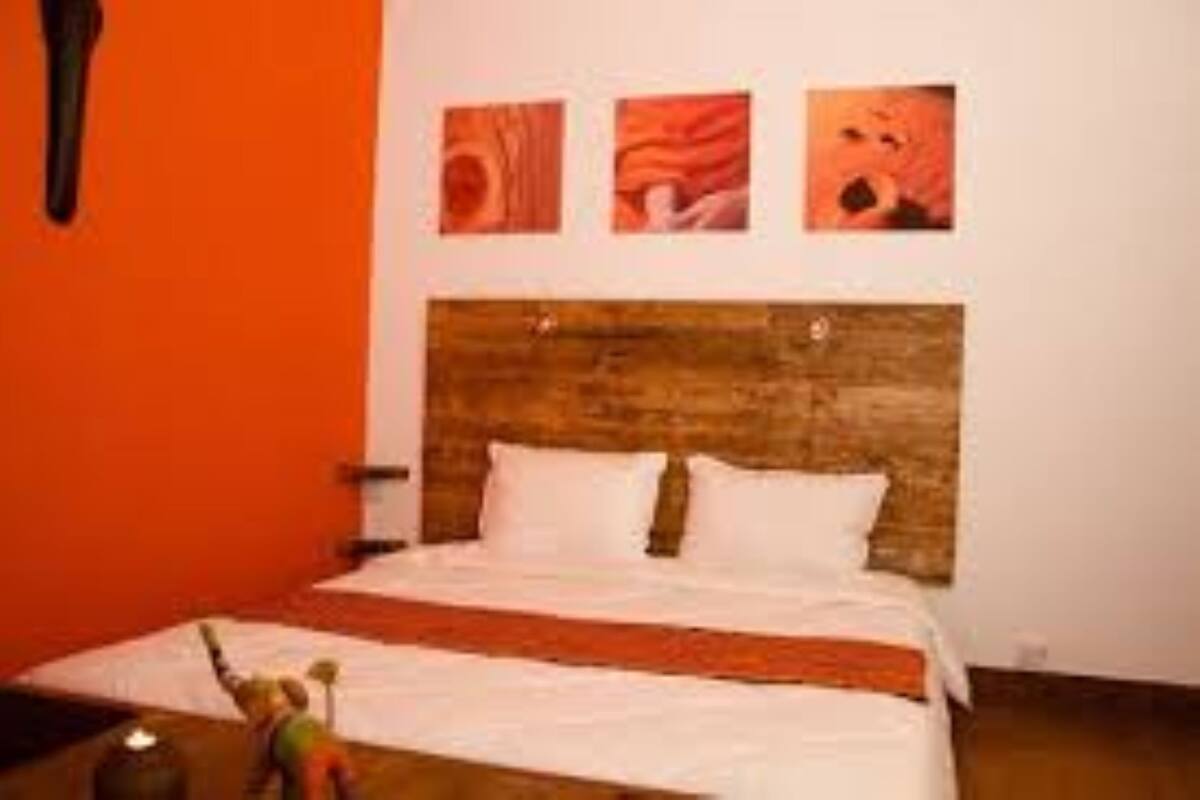 A hotel room with a wooden headboard, white bedding, and three framed artworks on the wall.