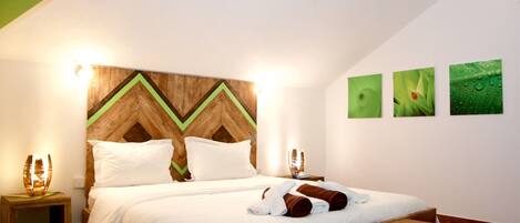 A neatly made bed with white linens and brown towels, a wooden headboard with a chevron pattern, and a small wooden table beside the bed.