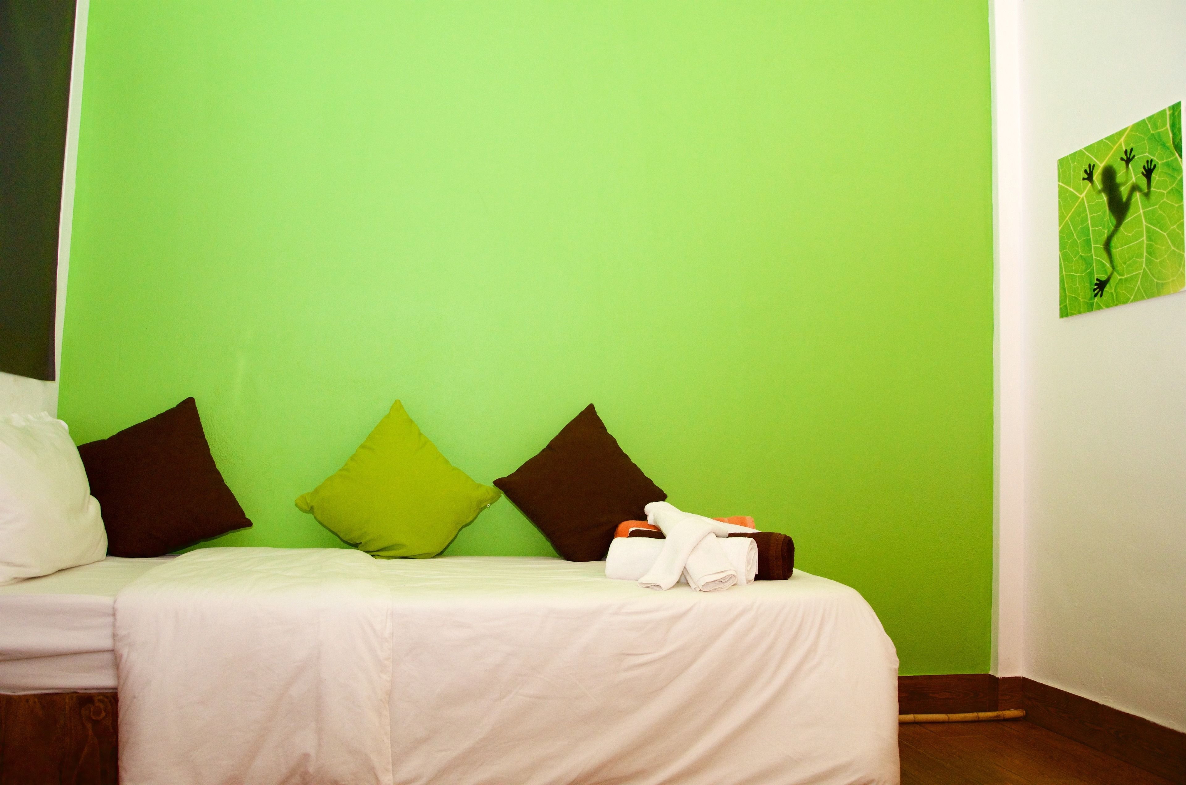 A hotel room with a green wall, a bed with white bedding, and two pillows.