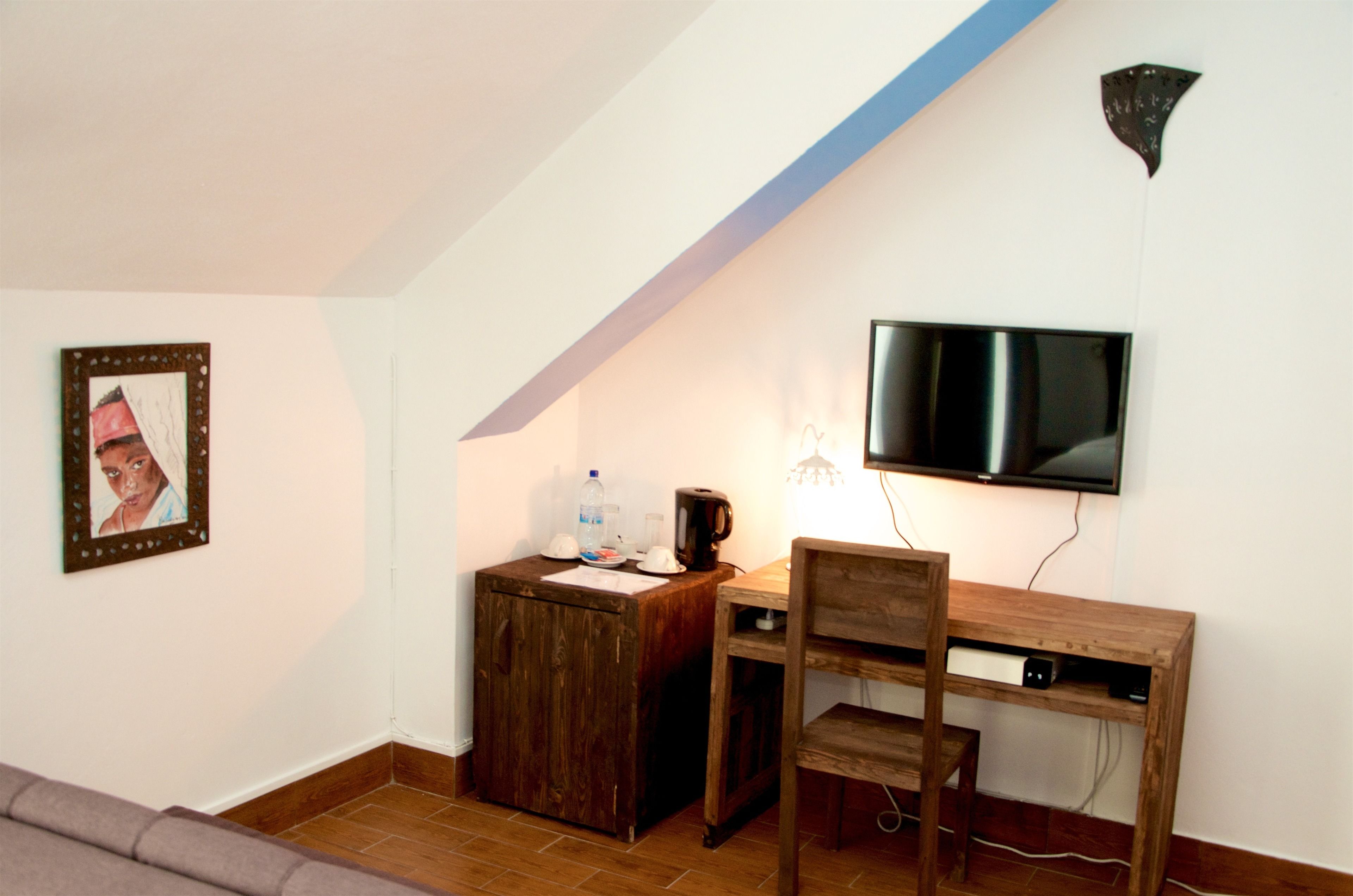 A small room with a wooden desk, a chair, a television mounted on the wall, and a framed picture on the wall.