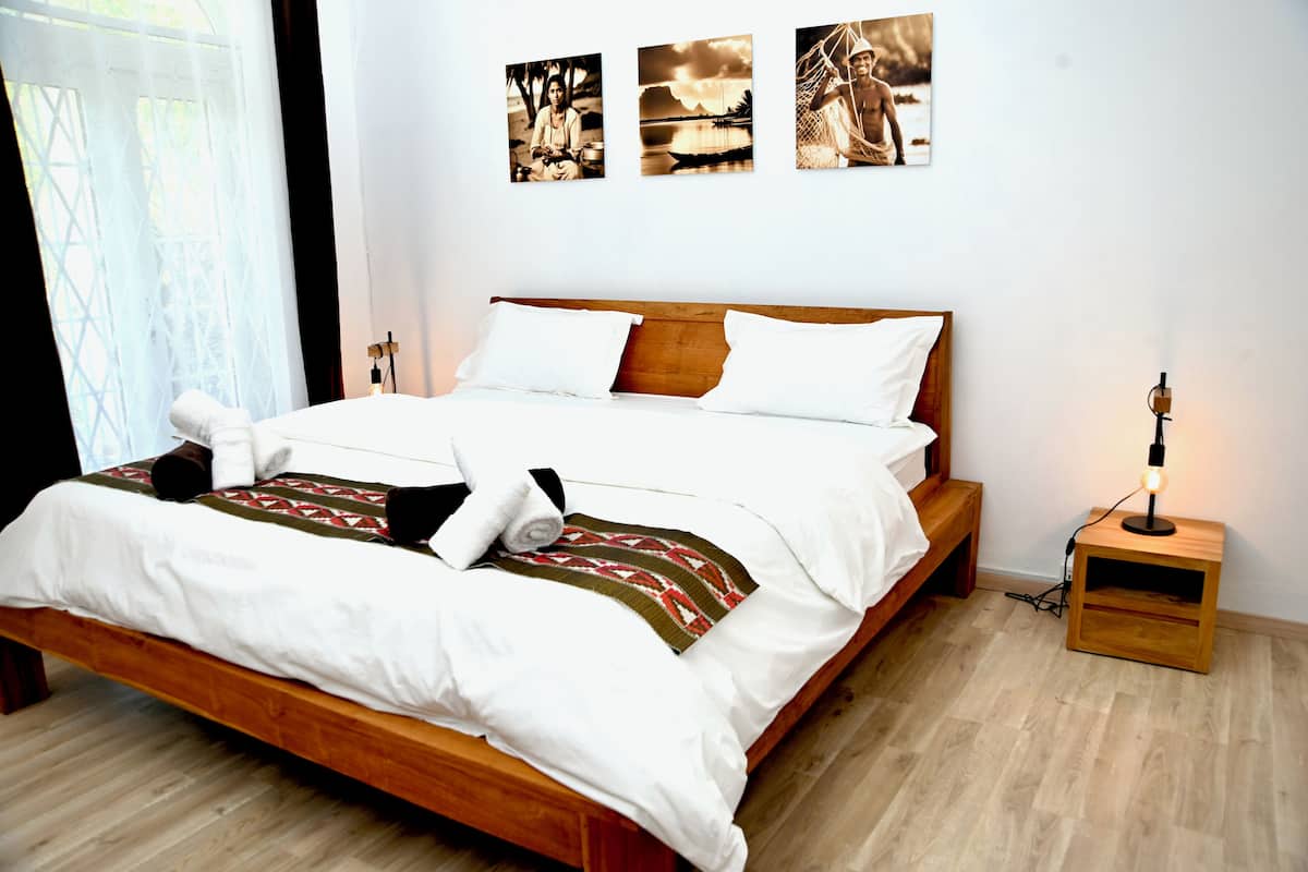 A neatly made bed with white linens and a patterned throw, a bedside table with a lamp, and three framed pictures on the wall.