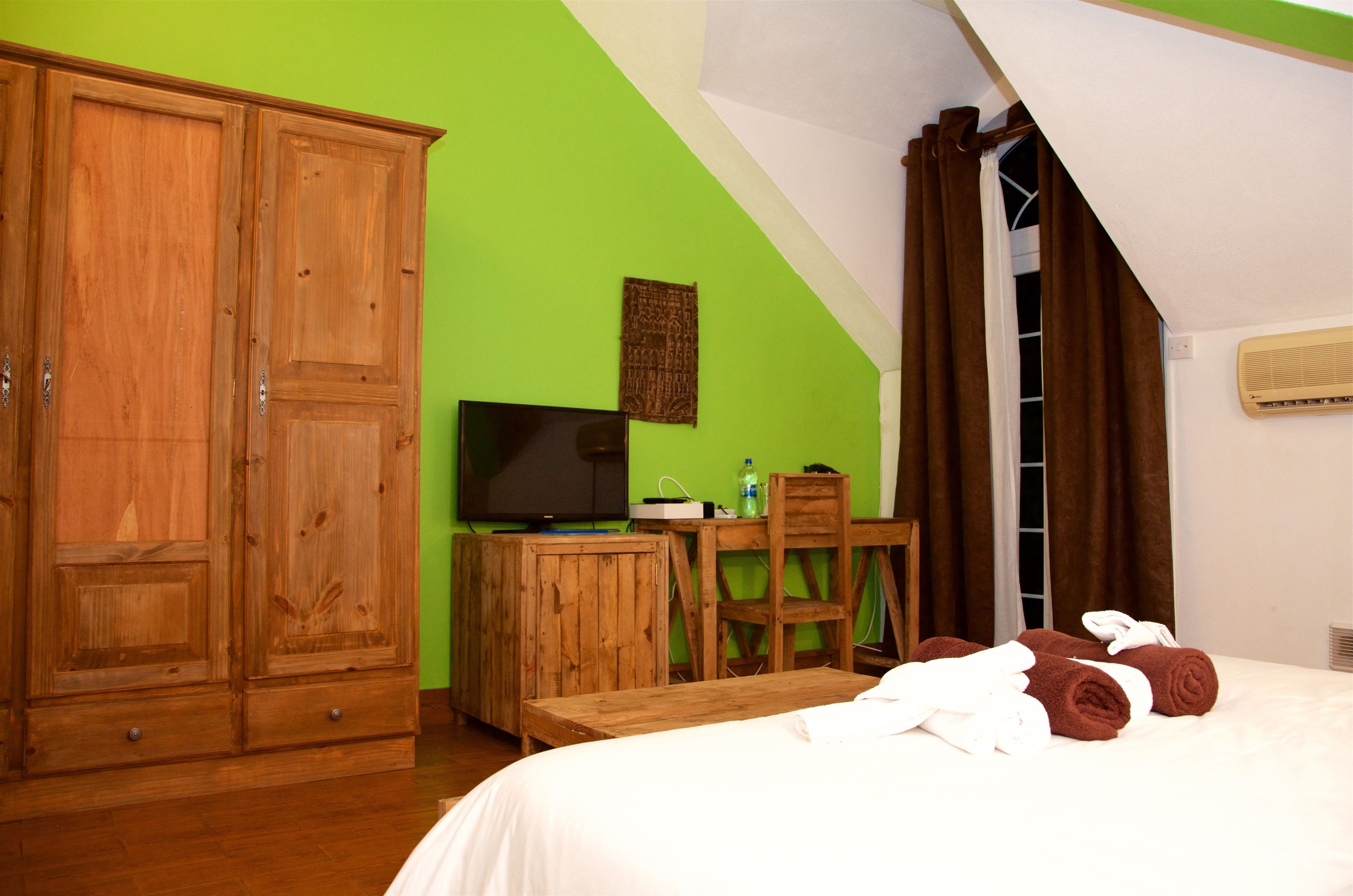 A room with a bed, wooden wardrobe, desk, chair, and a television.