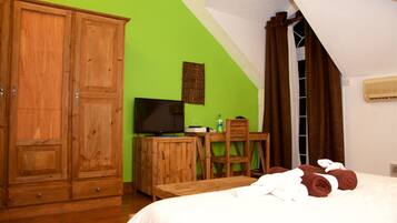 A room with a bed, wooden wardrobe, desk, chair, and a television.