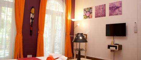 A hotel room with a bed, curtains, a television, artwork on the wall, and a lamp.