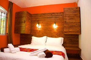 Une chambre d’hôtel avec une tête de lit en bois, du linge de lit blanc et une couvre-lit à motifs rouges.