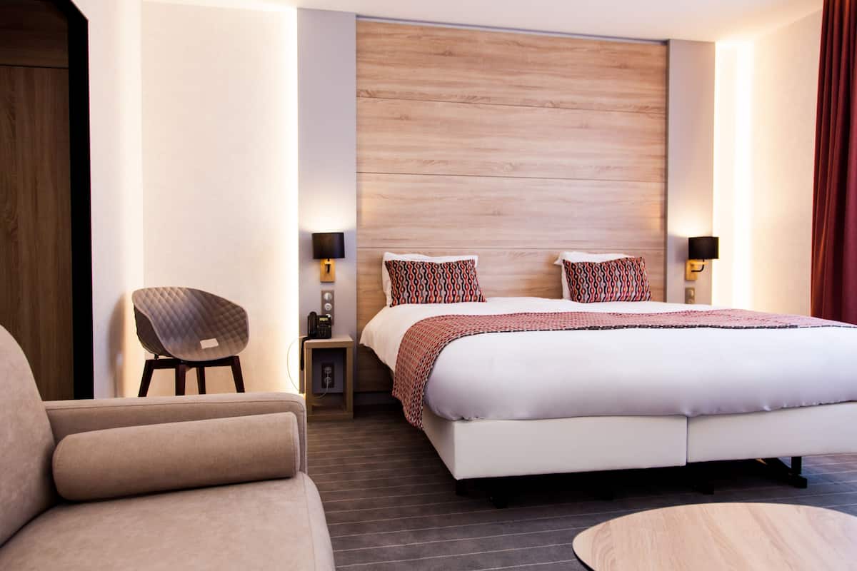 Una habitación de hotel moderna con una cama grande, una silla, una mesita de noche y una lámpara de pared.