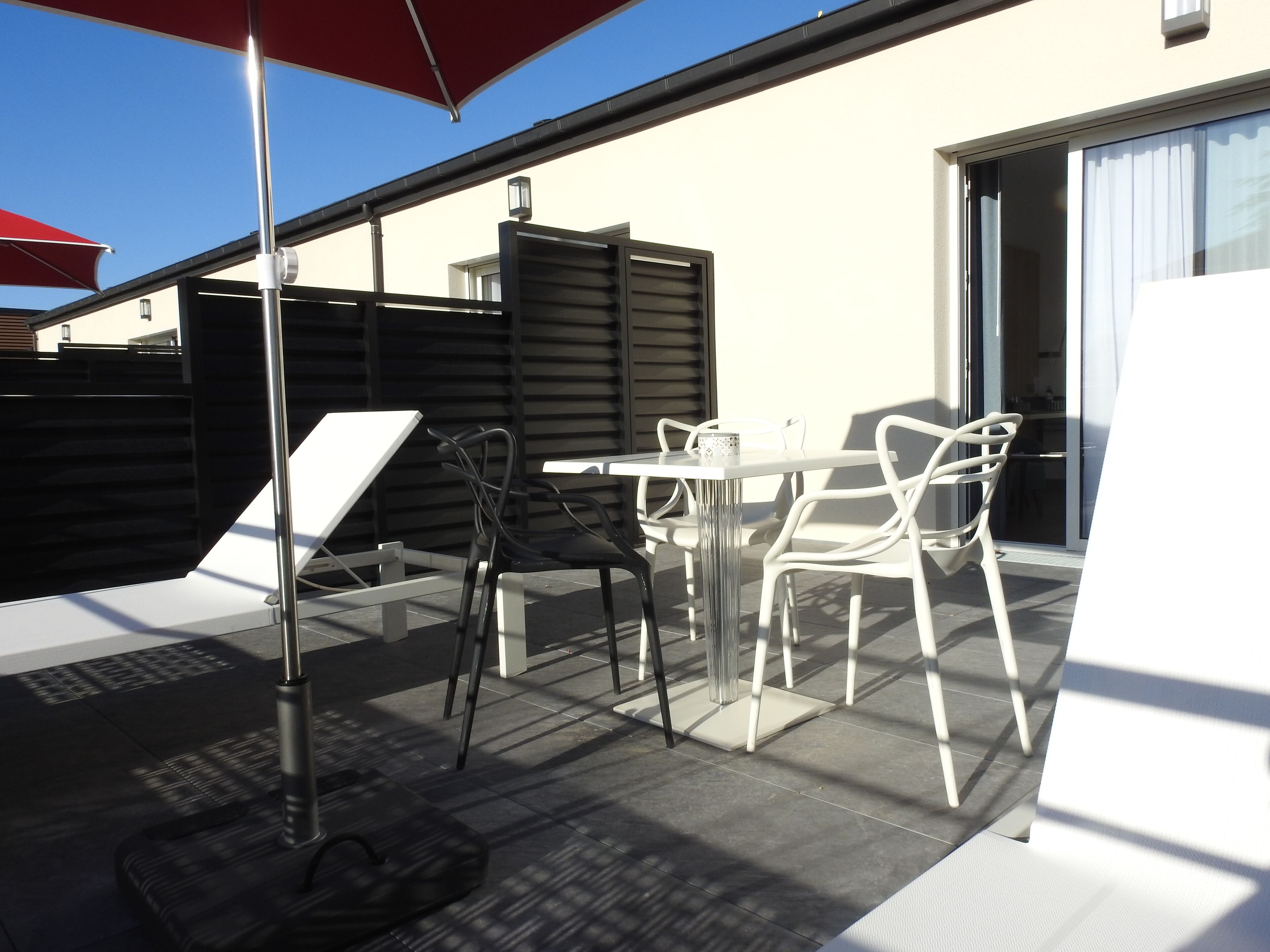 Un patio al aire libre con una mesa, sillas, un paraguas rojo y una bolsa negra en el suelo.