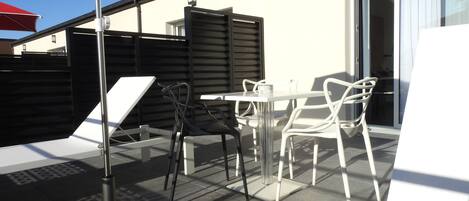 Un patio al aire libre con una mesa, sillas, un paraguas rojo y una bolsa negra en el suelo.