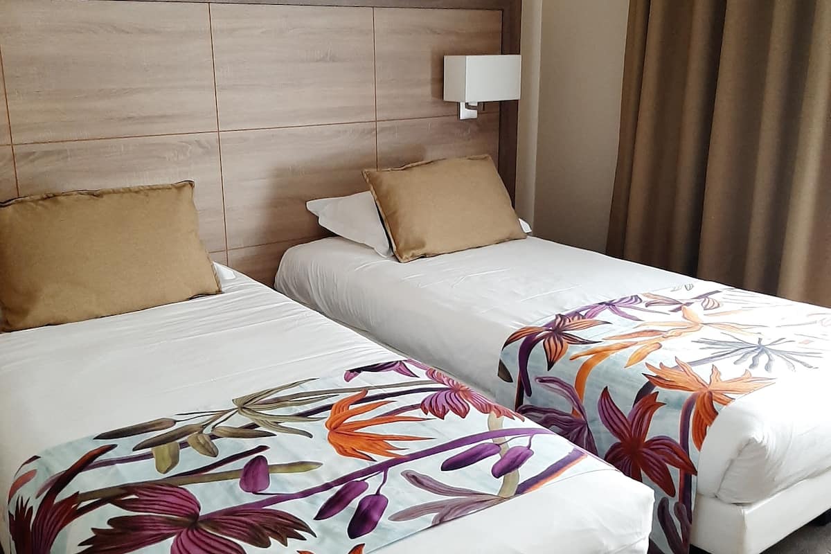 Una habitación de hotel con dos camas, cada una con colcha estampada y cabecero de madera, y una lámpara fijada a la pared.
