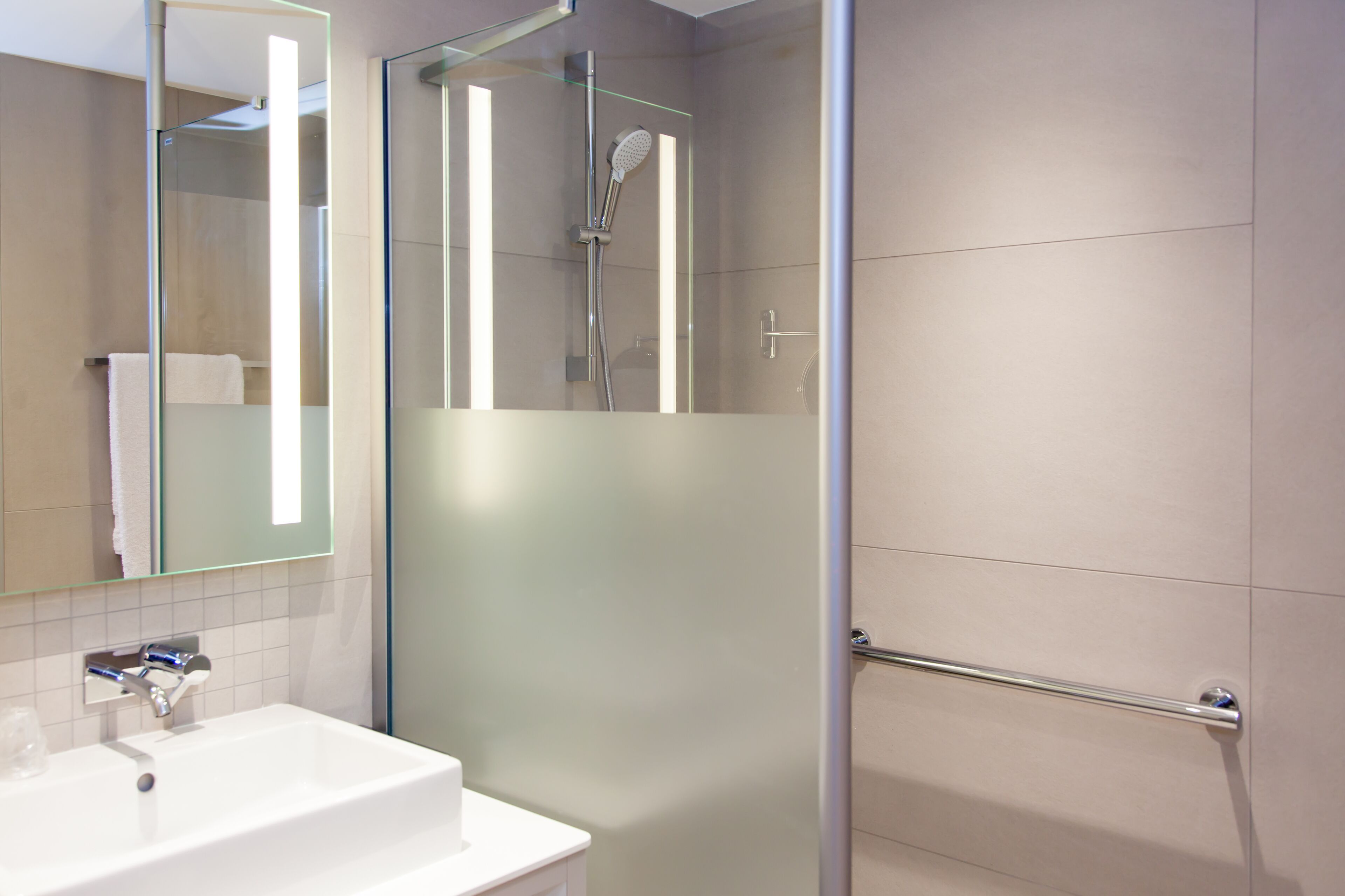 A modern bathroom with a glass-enclosed shower, a white sink, and a mirror.