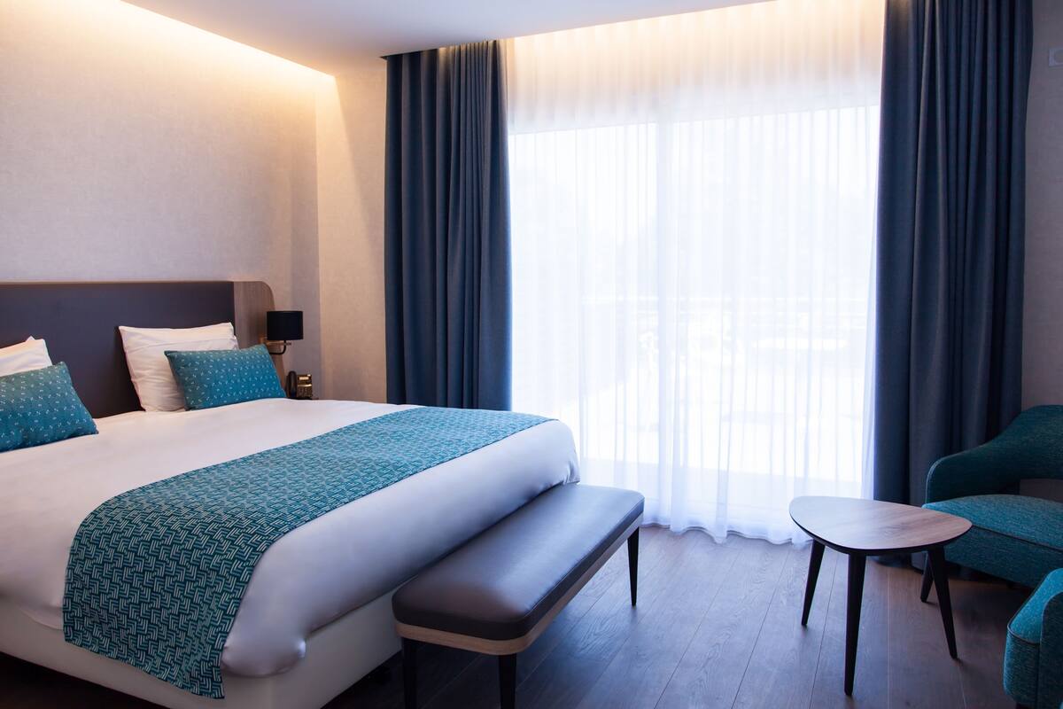 Una habitación de hotel con una cama grande, un banco, una mesita y una silla.