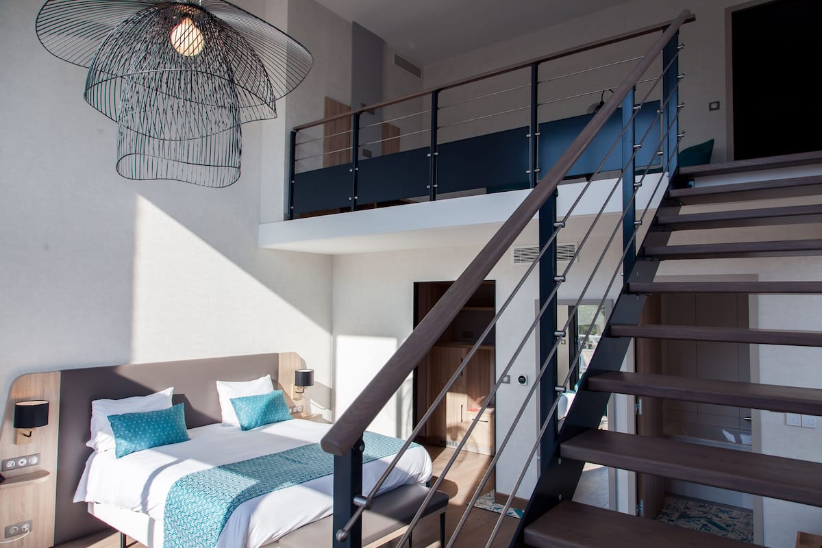 Una habitación de hotel moderna con una cama grande, un cabecero de madera, un balcón y una escalera.