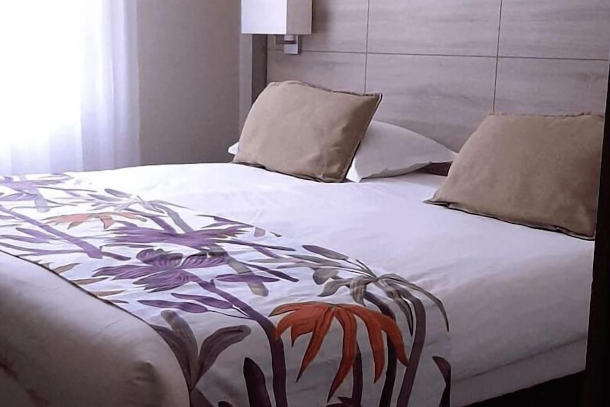 A hotel room with a bed, two pillows, and a floral-patterned bedspread.