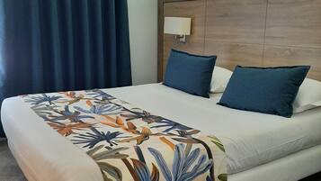A hotel room with a bed, a headboard, a bedside lamp, and a window with curtains.