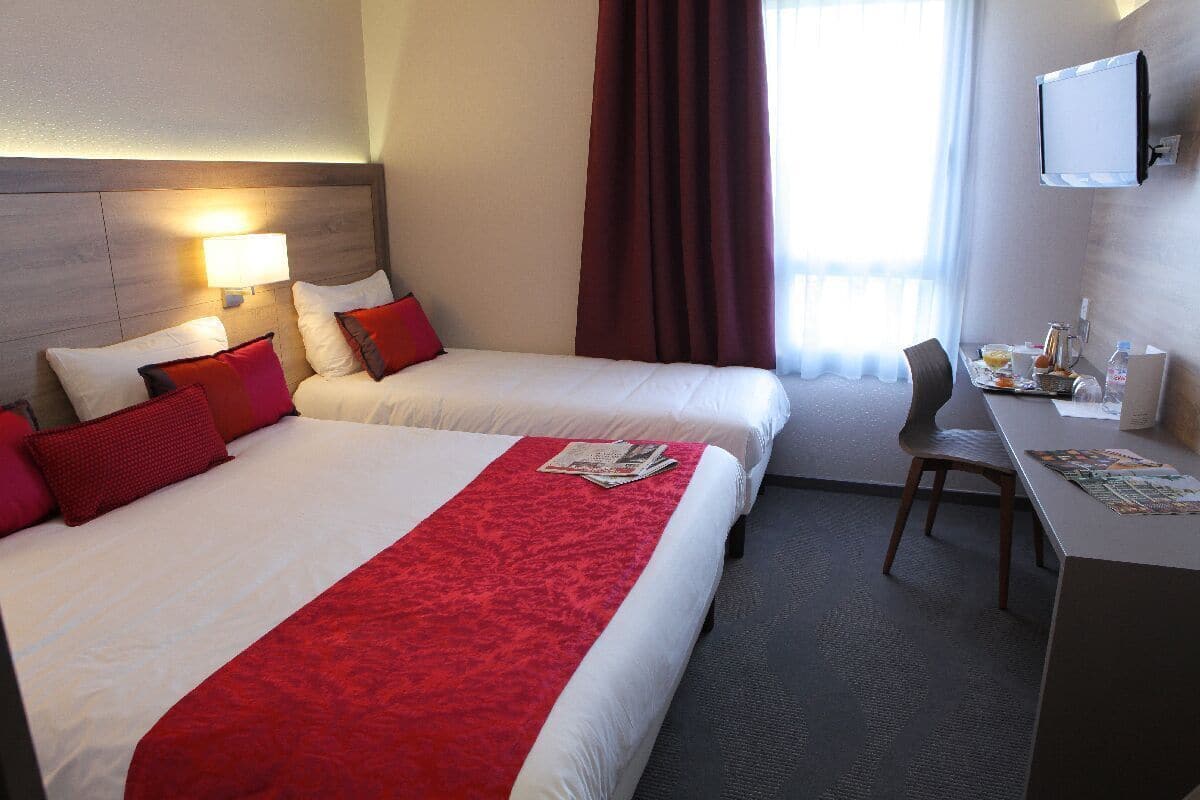 Habitación de hotel con dos camas, un escritorio, una silla, un televisor y una ventana con cortinas.