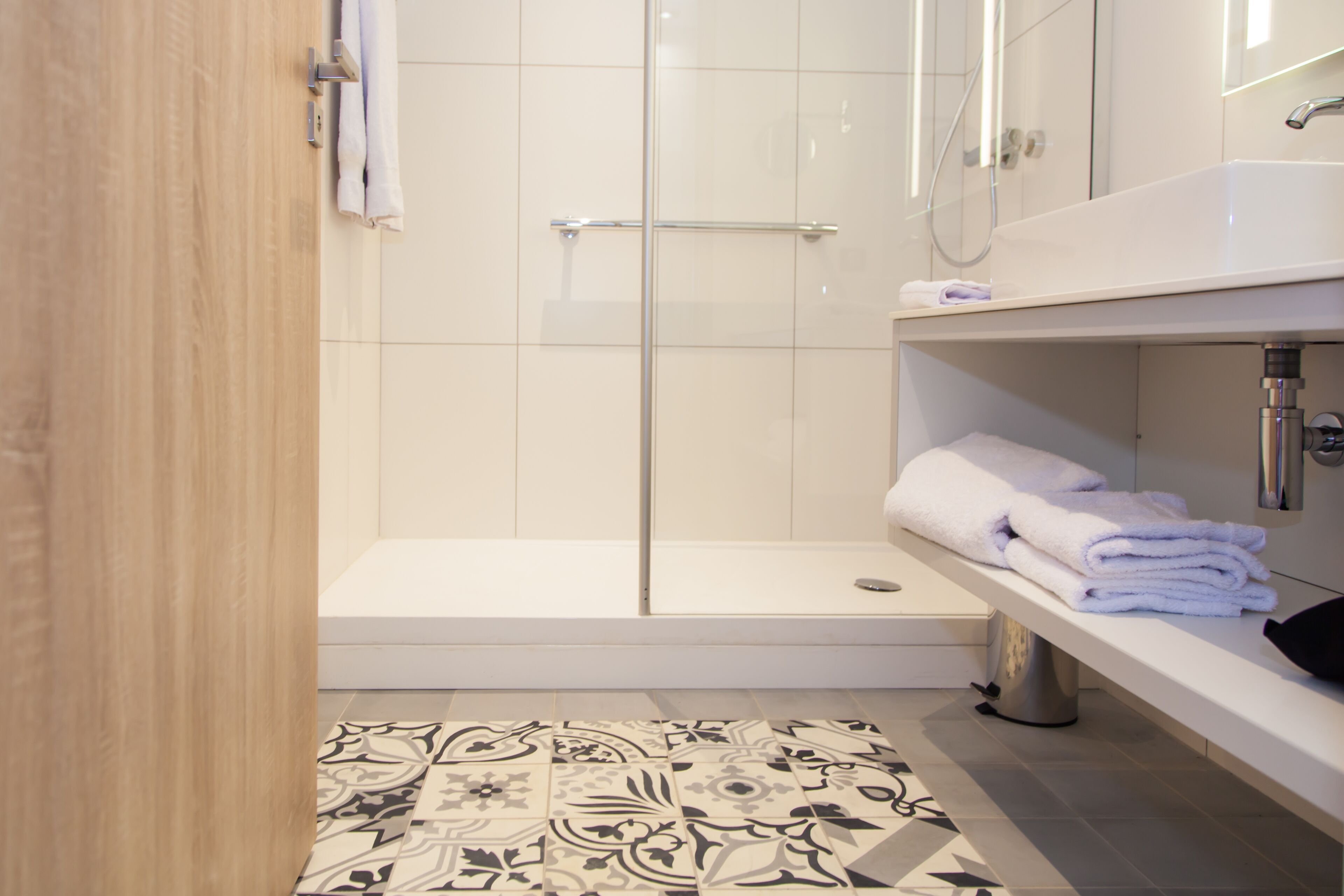 A modern bathroom with a glass shower enclosure, a white sink, and a patterned floor.