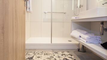 A modern bathroom with a glass shower enclosure, a white sink, and a patterned floor.