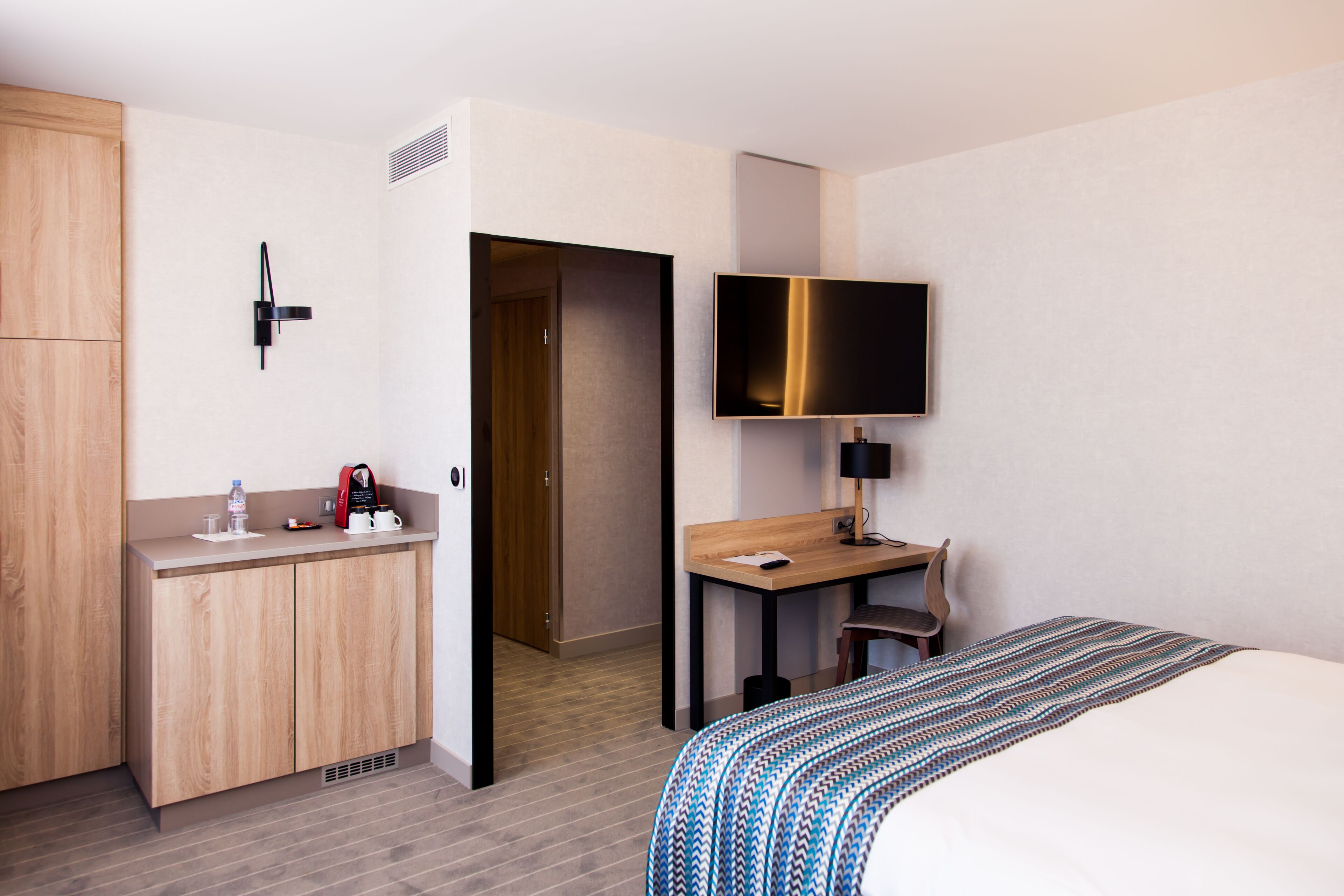A hotel room with a bed, a desk, a television, a wardrobe, and a bathroom.
