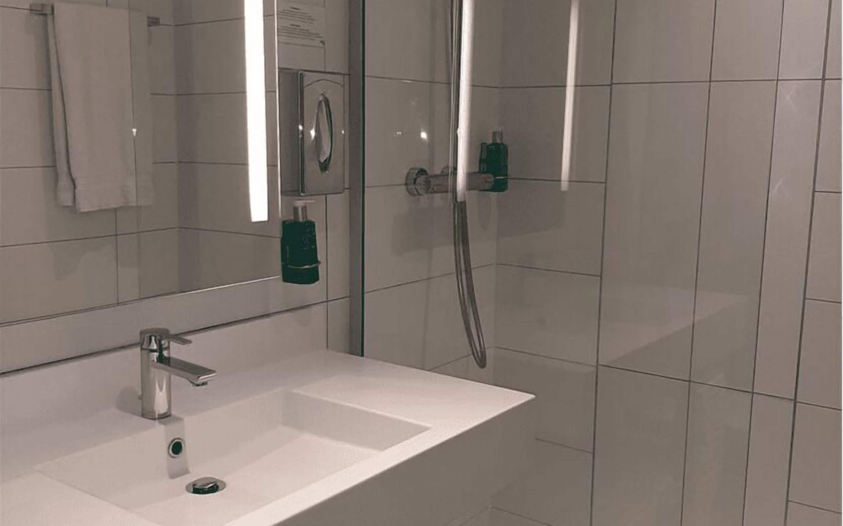 A bathroom with a white sink, a mirror, a shower, and a towel hanging on the wall.