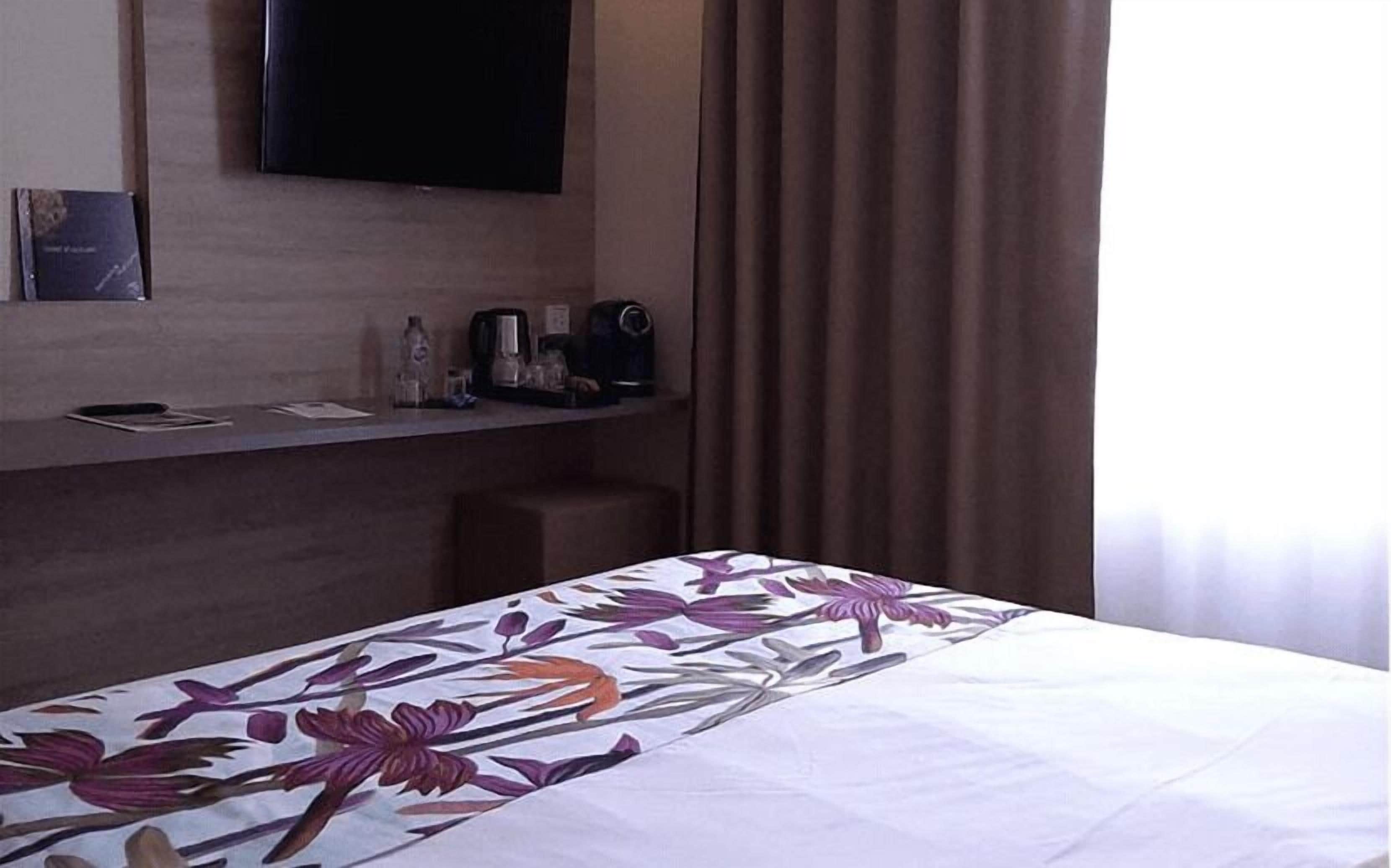 Una habitación de hotel con una cama, un televisor de pantalla plana montado en la pared, una cafetera y una mesita con bandeja.