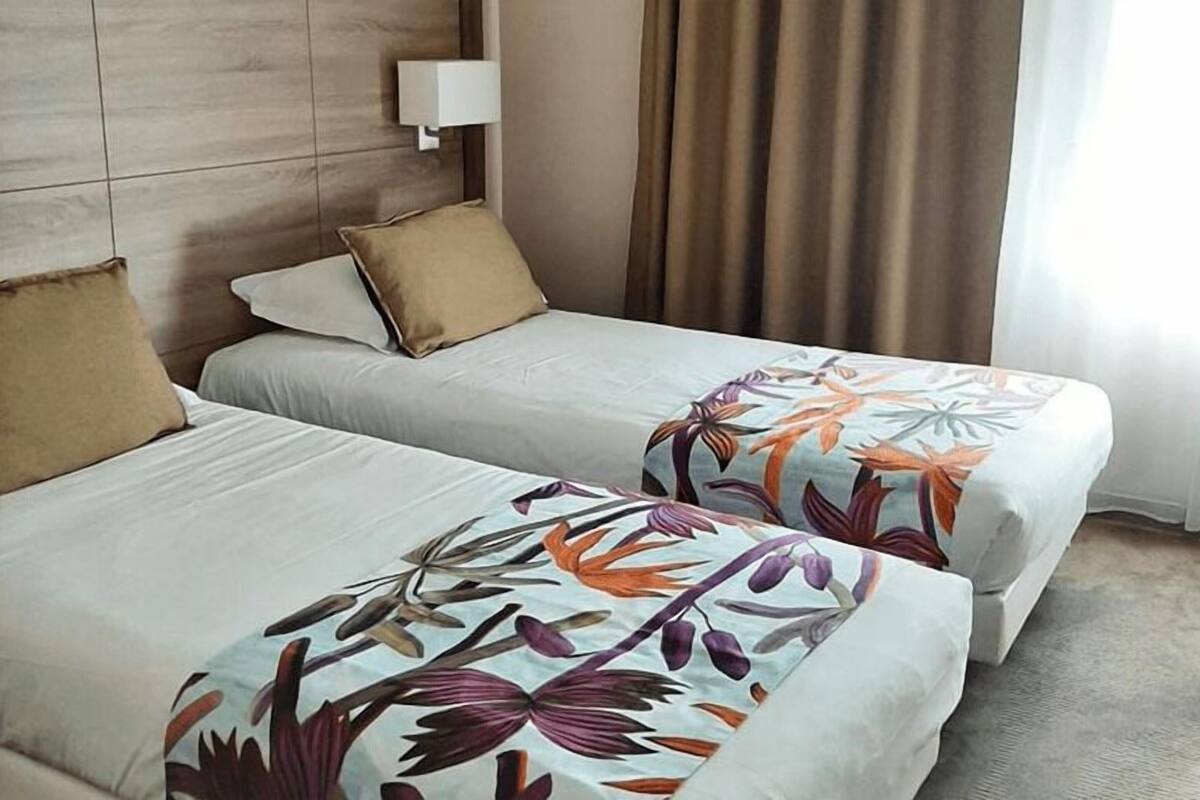 Dos camas individuales con cubrecamas estampados, una lámpara de noche y vistas a una cortina y ventana.