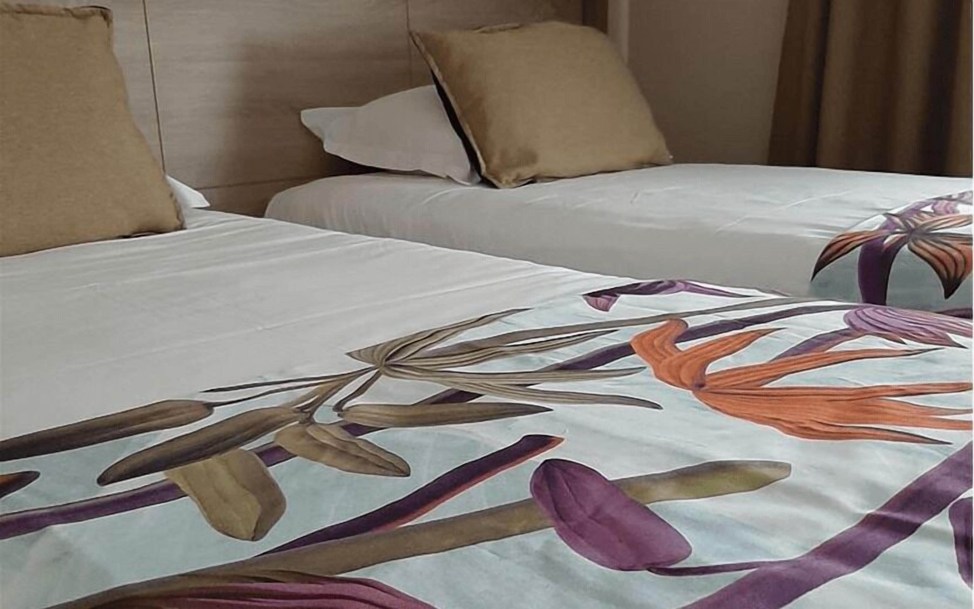 Een hotelkamer met twee bedden, elk met een witte spreidek en een beige kussen.