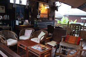 A rustic outdoor seating area with wicker furniture and a wooden table, surrounded by various items and decorations. - Boondee House (Mae Hong Son)