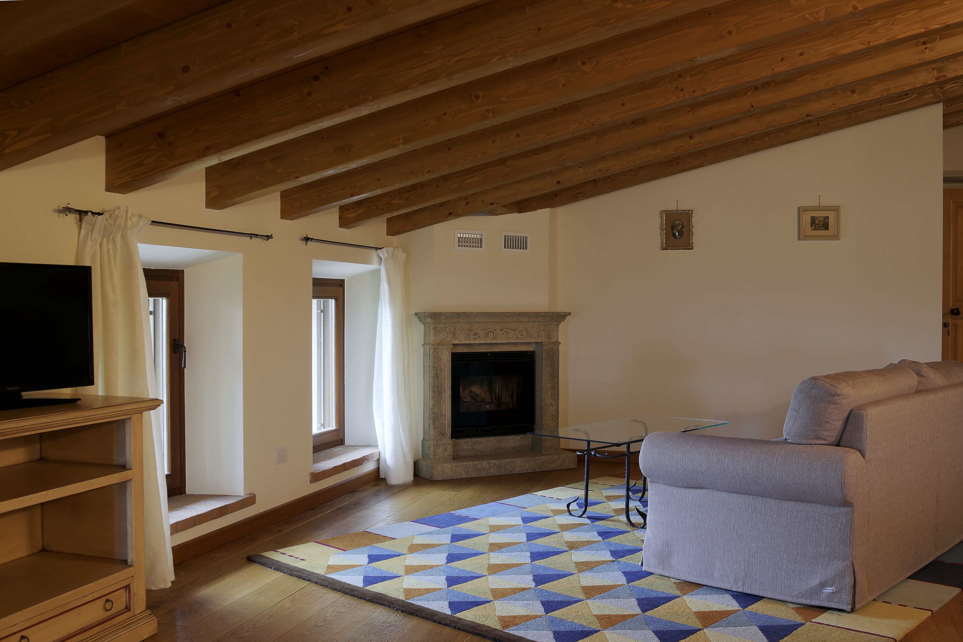 Un salon avec une cheminée, un canapé, un téléviseur posé sur un meuble en bois et un tapis à motifs.