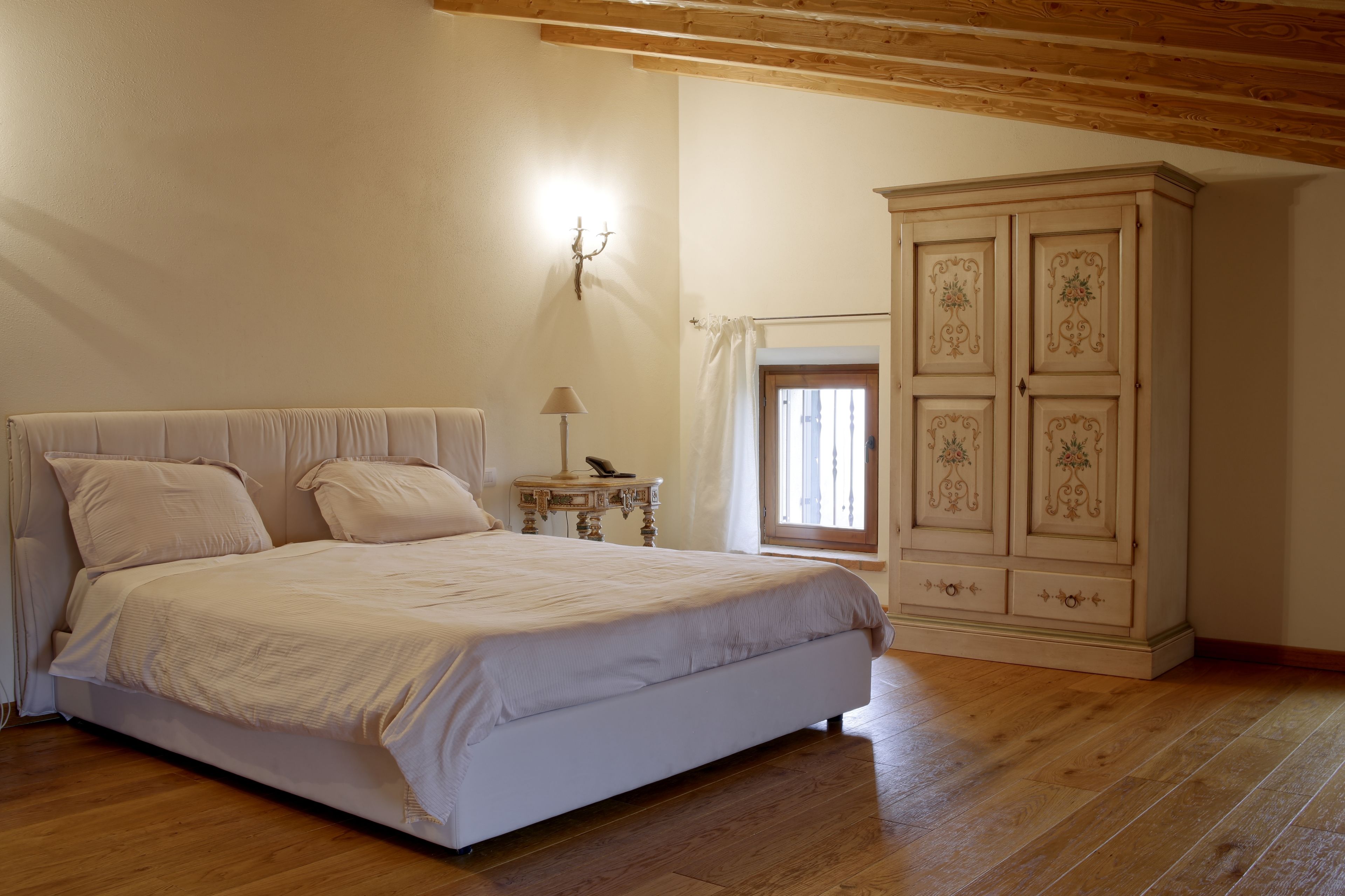 A bedroom with a large bed, wooden flooring, a wardrobe, and a window with curtains.