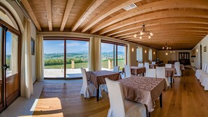 Un comedor amplio con techos de madera y ventanas grandes que ofrecen una vista panorámica. Las mesas están ordenadas con sillas blancas.