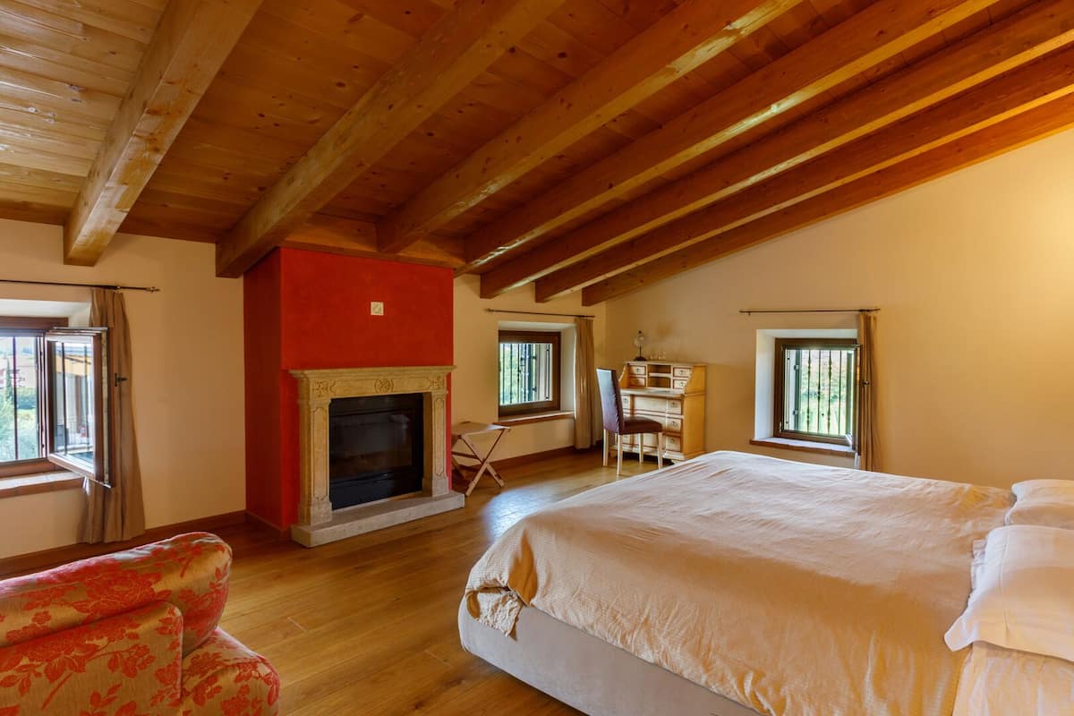 A bedroom with a large bed, a fireplace, a desk, and a window.