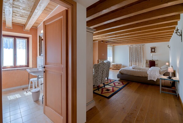 Una habitación con techo de madera, una cama, una mesita de noche, una lámpara, una silla, una alfombra y una ventana con cortinas.