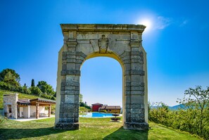 A stone archway leading to a pool area with a clear blue sky above.