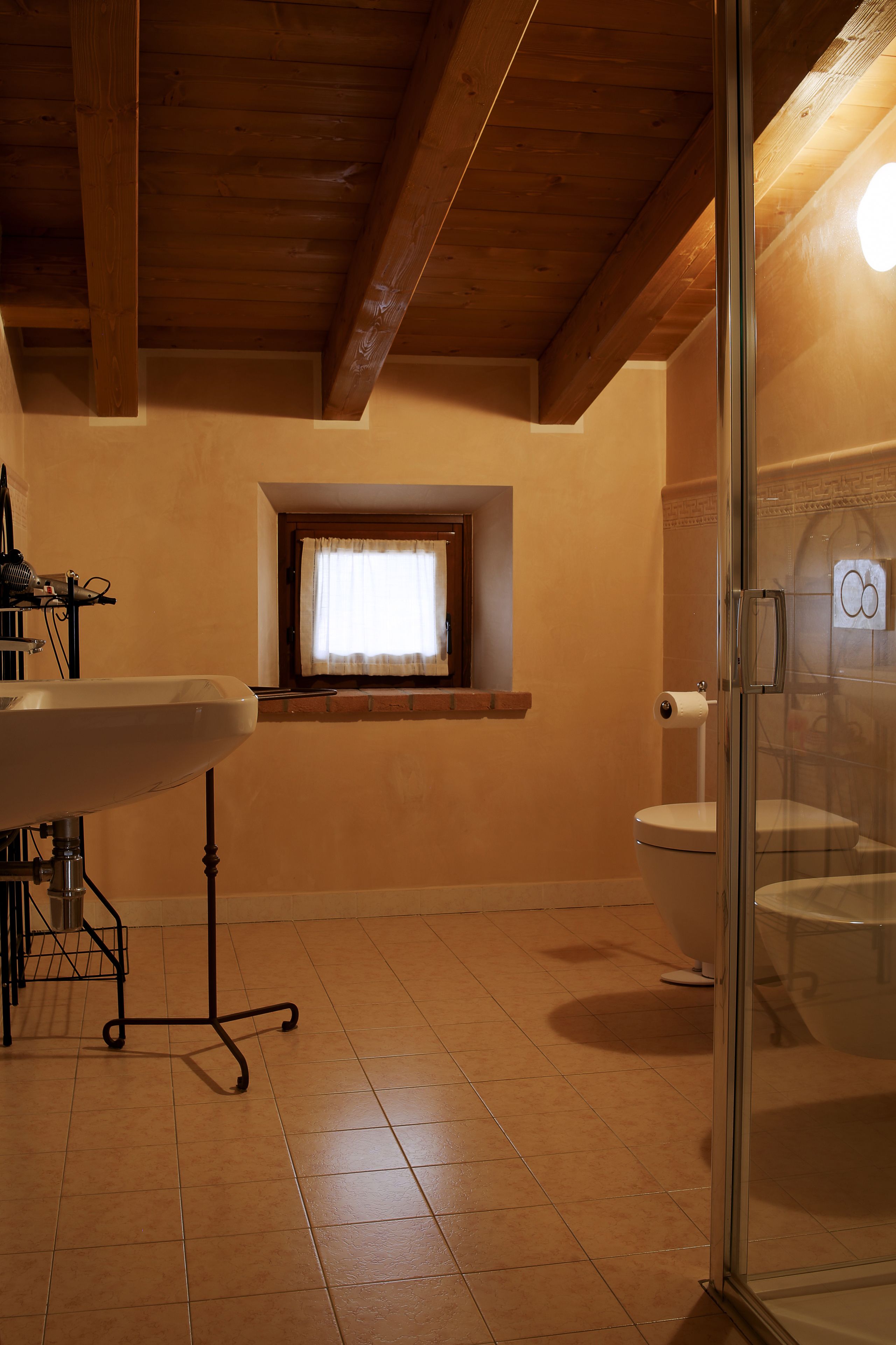 Une salle de bain avec un plafond en bois, une fenêtre avec un rideau, des toilettes et une cabine de douche en verre.