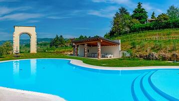 Ein Schwimmbecken mit einem Steingewölbe, einer überdachten Terrasse und einer sanften, grasbewachsenen Böschung.