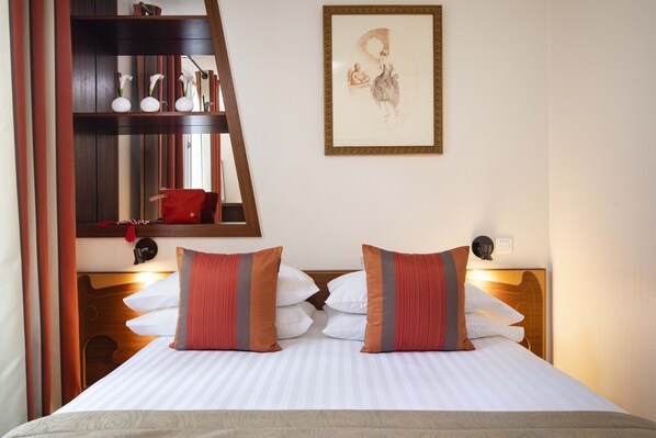 A neatly made bed with striped bedding, a wooden headboard, and two decorative pillows. - Grand Hotel des Balcons (Paris)