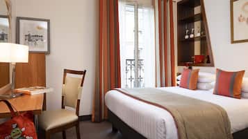 Ein Hotelzimmer mit Bett, Sessel, Schreibtisch, Lampe, einer Ablage mit Dekoration und einem Fenster mit Vorhängen.