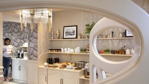 Una cocina moderna con armarios blancos, una araña y diversos productos para el desayuno sobre la encimera.