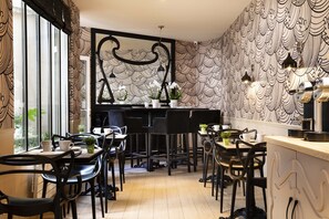 A modern cafe with black and white patterned wallpaper, black chairs, and a counter with a coffee machine. - Grand Hotel des Balcons (Paris)