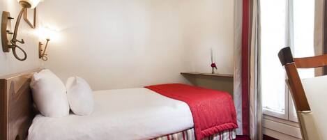 A hotel room with a single bed, a nightstand, a lamp, a chair, and a window with curtains.
